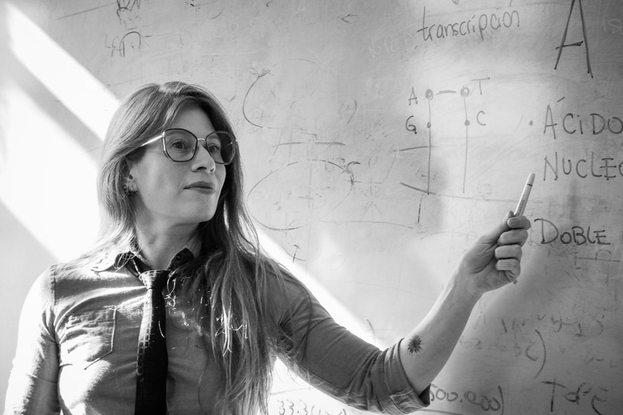 Female teacher giving a science lesson, explaining concepts on a whiteboard in black and white.